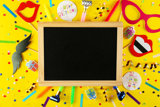 Photo booth props, blank blackboard, paper moustache, lips & glasses on stick. Party kit for birthday, wedding or corporate event celebration. Bright yellow background, flat lay, copy space, top view.