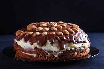 Homemade chocolate cake with milk cream and almonds on black wooden background.