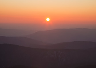 sunrise in the Carpathians on the background of blue mountain ranges and solar disk on the horizon. 