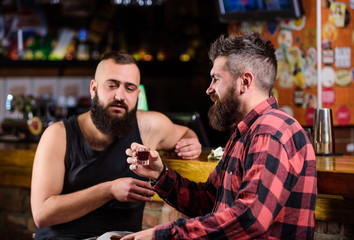 Friday relax in pub. Friends relaxing in pub. Drunk conversation. Cheers concept. Hipster brutal bearded man drinking alcohol with friend at bar counter. Men relaxing at pub. Strong alcohol drinks