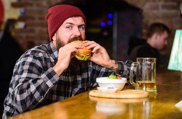High calorie food. Delicious burger concept. Enjoy taste of fresh burger. Hipster hungry man eat burger. Man with beard eat burger menu. Brutal hipster bearded man sit at bar counter. Cheat meal