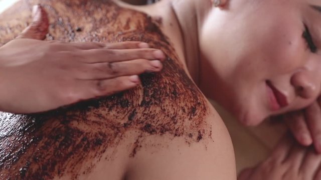 beautiful woman in spa salon getting massage treatment using coffee scrub