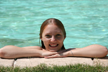 Smiling girl with hands outstretched enjoying sunbathing near swimming pool