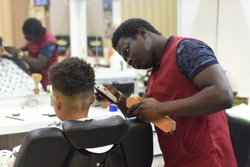 Cute african american boy in the african barbershop. Cute mixed boy makes a haircut in the African...