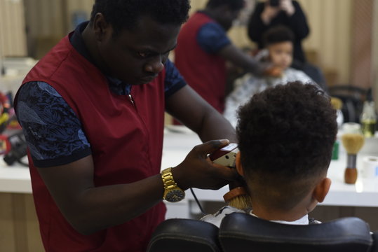 Cute african american boy in the african barbershop. Cute mixed boy makes a haircut in the African salon. Hair style. Haircut by machine for children. School boy hair style. Haircut by scissors. 
