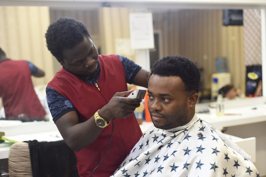 Black man in the african barbershop. Cute black man makes a haircut in the African salon. Hair style. Haircut by machine for adults. 