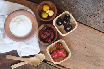 Natural homemade plain organic yogurt mixed with fresh berry fruit white bowl and wood spoon on wood texture background