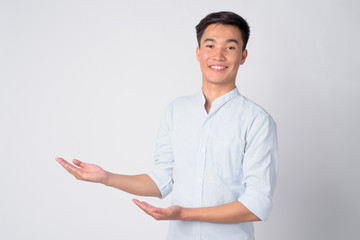 Portrait of young happy Asian businessman showing something