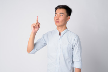Portrait of young handsome Asian businessman thinking and pointing up