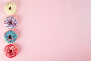 Top view composition of lush donut with colorful sprinkled icing, on bright paper textured background with a lot of copy space for text. Tasty but unhealthy food concept. Close up, flat lay, frame.