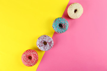 Top view composition of lush donut with colorful sprinkled icing, on bright paper textured background with a lot of copy space for text. Tasty but unhealthy food concept. Close up, flat lay, frame.