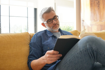 Man in 40s reading book in modern home - obrazy, fototapety, plakaty