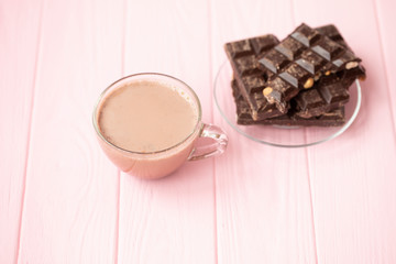 Cup of cocoa and dark chocolate on a pink wooden background