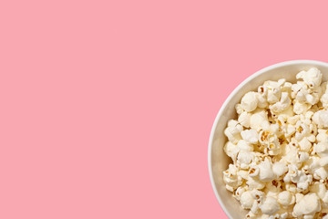 Popcorn in bowl on pink background with copy space.