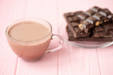 Cup of cocoa and dark chocolate on a pink wooden background