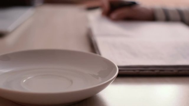 The girl writes tasks for the day in a notebook. Mug with drink in the background.