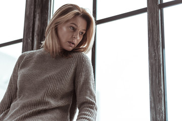 Stressed woman wearing sweater sitting near the window