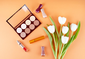 Cosmetics and flowers lies on a soft peach background. Contents of women's cosmetic bag