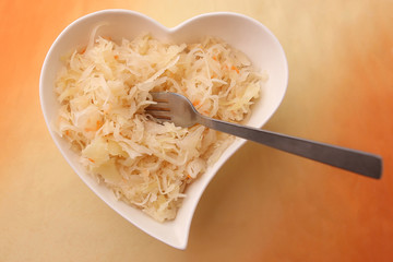 Sauerkraut in heart shaped plate. Marinated cabbage in plate with fork on orange background.