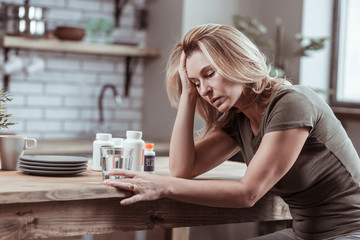 Blonde-haired woman sitting in kitchen and taking medicine