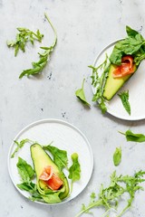 Ripe avocado boats with slices of salted trout, salmon and fresh greens on a gray background. Avocado boats stuffed with salmon with lime, spinach leaves and arugula, concept healthy food, diet.