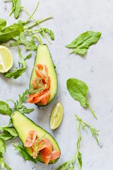 Ripe avocado boats with slices of salted trout, salmon and fresh greens on a gray background. Avocado boats stuffed with salmon with lime, spinach leaves and arugula, concept healthy food, diet.