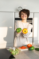 Happy young woman cooking fresh salad at the kitchen