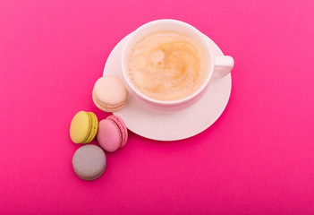 Cozy morning breakfast. Cup of coffee and colorful macaron on pink background top view. Fashion flat lay. Sweet macaroons.