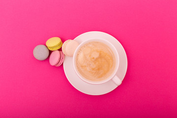 Cozy morning breakfast. Cup of coffee and colorful macaron on pink background top view. Fashion flat lay. Sweet macaroons.