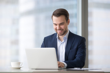 Fototapeta na wymiar Happy businessman in suit using laptop software at workplace