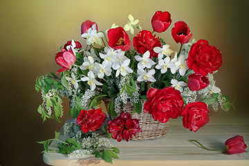 Beautiful bouquet of spring flowers in a basket.Still life with red tulips and daffodils .
