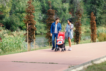 Obraz premium mom and dad are walking in the park with their daughter in a stroller, a beautiful sunny day, a beautiful family