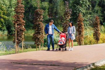 mom and dad are walking in the park with their daughter in a stroller, a beautiful sunny day, a...