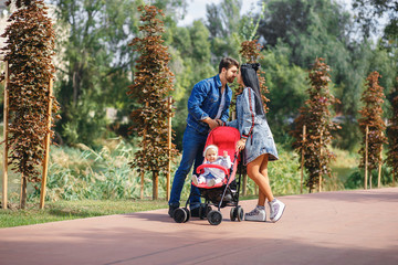 mom and dad are walking in the park with their daughter in a stroller, a beautiful sunny day, a beautiful family