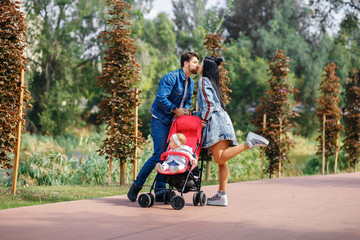 Obraz premium mom and dad are walking in the park with their daughter in a stroller, a beautiful sunny day, a beautiful family
