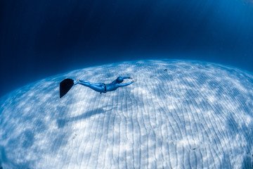 Woman freediver in monofin glides in the sea over the sandy bottom (sea eels are visible in the...