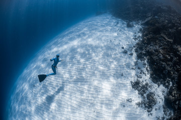 Woman freediver in monofin hangs in the sea over the sandy bottom
