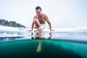 Young man with lean and muscular body ready to dive into the ice hole and to perform recreational...