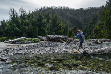 Naklejka premium Woman hiker crossing the small river in the wild area