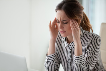 Tired stressed businesswoman feeling strong headache massaging temples in office