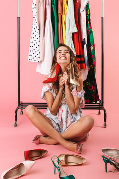 Full length photo of cheerful woman in dress sitting under wardrobe rack with shoes