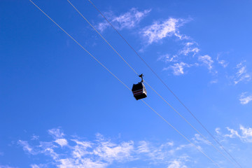Naklejka na ściany i meble Bottom view of cable car on blue sky background. Cable car going down along the cliffs.
