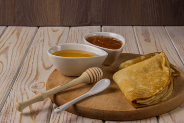 Pancakes on a wooden board with honey and jam