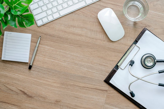 Doctor working desk concept, white keyboard, mouse, chart and stethoscope on wooden table.