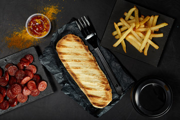 Grilled bun, sausages, french fries and cup of coffee to go on black background