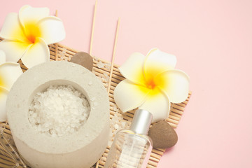 Bottles with aromatic oils, sea salt, tropical flowers plumeria on a pink background. Spa treatments concept, sauna, massage. Flat lay, top view.