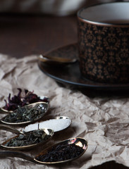 Black tea cup with golden spoons and green, black and carcade tea, drink and beverage photo in dark mood and craft style photo