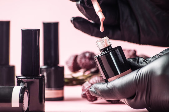 Nail salon: the master's hand in a black glove is dipping a brush with a drop in nail polish.