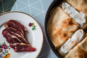 Food preparing in a countryside. Stuffed pancakes, cream and dried meat.