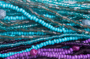 Abstract bead background - Top view photo of many strings of purple and turquoise glass beads close...